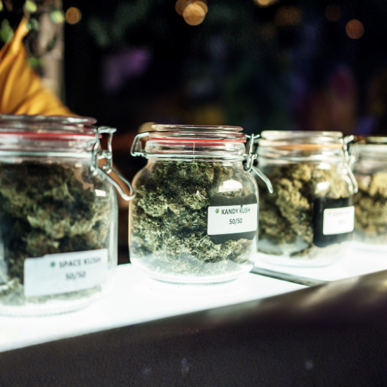 Glass jars filled with cannabis buds labeled Space Kush and Kandy Kush on display under bright light.