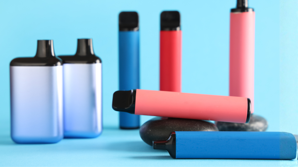 Colorful disposable vapes in pink and blue on stones with blue background for vaping products.