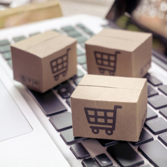 Mini shipping boxes with shopping cart icons on laptop keyboard for online ecommerce concept.